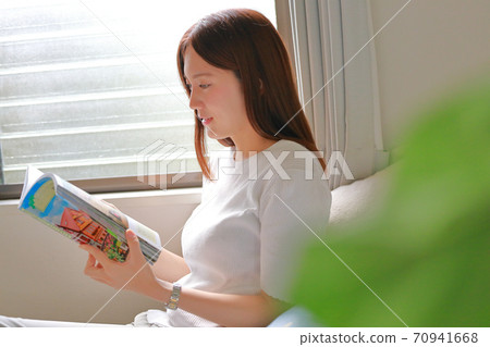 Woman looking at a book by the window 70941668
