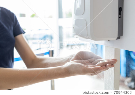 Hands of girl using automatic alcohol gel dispenser,spraying on hands,clean hands with alcohol hand sanitizer machine,antiseptic, disinfectant to kill germs,new normal life under Coronavirus,COVID-19 70944303