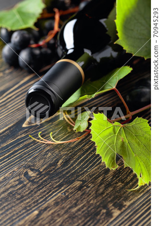 Unopened red wine bottle, vine twig, and ripe grapes on an old wooden table. 70945293