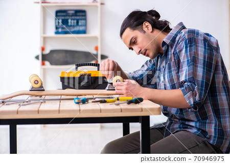 Young man repairing skateboard at workshop 70946975
