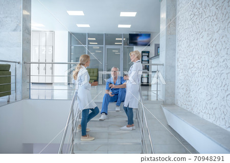 Team of medical workers resting, drinking coffee on stairs Team of medical workers resting, drinking coffee on stairs 70948291