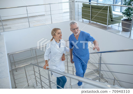 Male and female doctors walking upstairs, having friendly conversation Male and female doctors walking upstairs, having friendly conversation 70948310