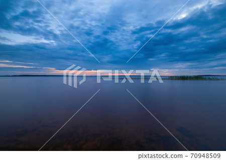 Blue tranquil landscape with calm water and cloudy sky Blue tranquil landscape with calm water and cloudy sky 70948509
