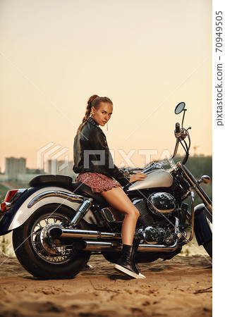 Biker girl in a leather jacket on a motorcycle looking at the sunset. Biker girl in a leather jacket on a motorcycle looking at the sunset. 70949505
