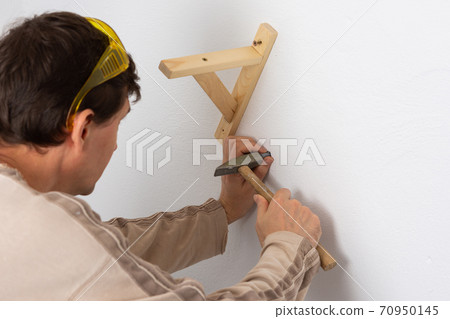 Worker scores plastic anchor with a hammer Worker scores plastic anchor with a hammer 70950145