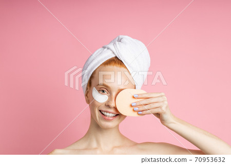 Shot of young woman applies eye patches and holding cosmetic sponge Shot of young woman applies eye patches and holding cosmetic sponge 70953632