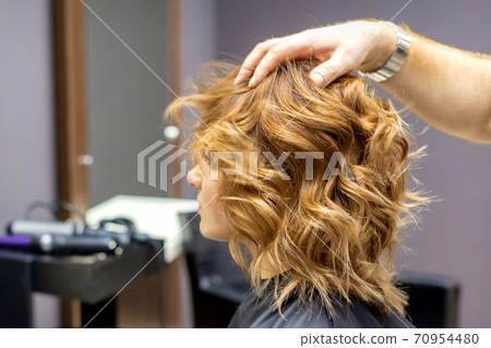 Hairdresser checks curly hairstyle of woman 70954480