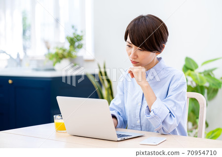 A middle-aged woman teleworking in the living room. A middle-aged woman teleworking in the living room. 70954710