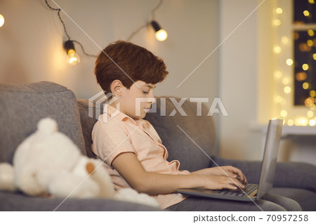 Boy sitting on sofa with laptop and typing message during online communication Boy sitting on sofa with laptop and typing message during online communication 70957258