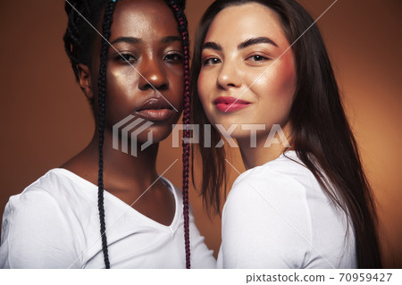 young pretty caucasian, afro woman posing cheerful together on brown background, lifestyle diverse nationality people concept young pretty caucasian, afro woman posing cheerful together on brown background, lifestyle diverse nationality people concept 70959427