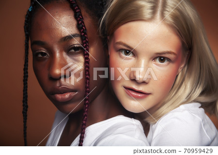 two pretty girls african and caucasian blond posing cheerful together on brown background, ethnicity diverse lifestyle people concept two pretty girls african and caucasian blond posing cheerful together on brown background, ethnicity diverse lifestyle people concept 70959429