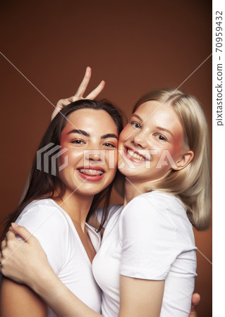 two pretty diverse girls happy posing together: blond and brunette on brown background, lifestyle people concept two pretty diverse girls happy posing together: blond and brunette on brown background, lifestyle people concept 70959432