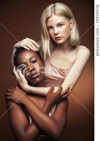 two pretty girls african and caucasian blond posing cheerful together on brown background, ethnicity diverse lifestyle people concept 70959438