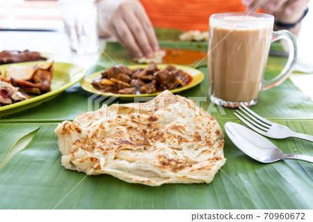 Roti canai or paratha served on banana leaf, with mutton curry and fried chicken, and popular teh tarik 70960672