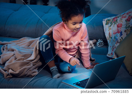 Happy african-american little girl during video call with laptop and home devices, looks delighted and happy 70961885