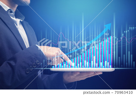Man in suit holds tablet with futuristic hologram graphic and works at growth chart Man in suit holds tablet with futuristic hologram graphic and works at growth chart 70963410