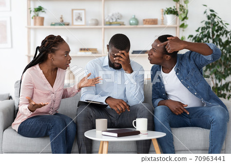 Tired Psychotherapist Sitting On Couch Between Quarreling Couple During Therapy Session 70963441