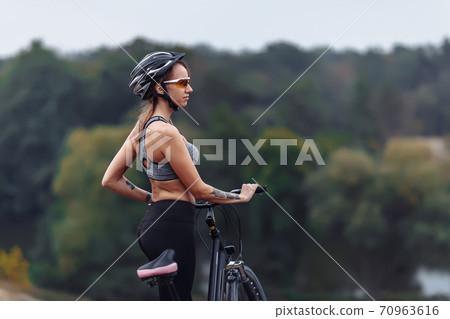 Fit young woman wearing sportswear standing with her bicycle on rocky background Fit young woman wearing sportswear standing with her bicycle on rocky background 70963616