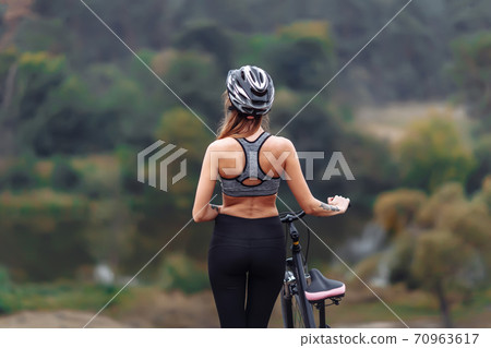 Fit young woman wearing sportswear standing with her bicycle on rocky background Fit young woman wearing sportswear standing with her bicycle on rocky background 70963617