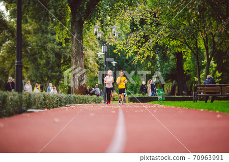 Active recreation and sports children in pre-adolescence. Caucasian twins boy and girl 10 years old jogging on red rubber track through park. Children brother and sister running on treadmill outside Active recreation and sports children in pre-adolescence. Caucasian twins boy and girl 10 years old jogging on red rubber track through park. Children brother and sister running on treadmill outside 70963991