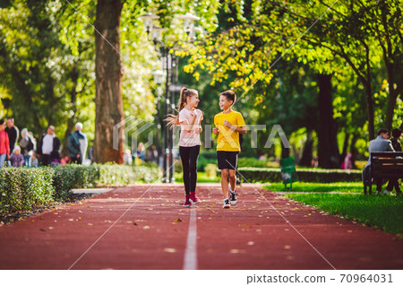 Sports and fitness in adolescence. Caucasian twins boy and girl run on the jogging track in the city park. Two children brother and sister for 10 years running on a rubberized outdoor treadmill Sports and fitness in adolescence. Caucasian twins boy and girl run on the jogging track in the city park. Two children brother and sister for 10 years running on a rubberized outdoor treadmill 70964031