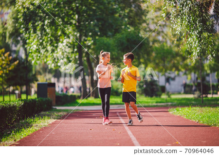 Active recreation and sports children in pre-adolescence. Caucasian twins boy and girl 10 years old jogging on red rubber track through park. Children brother and sister running on treadmill outside Active recreation and sports children in pre-adolescence. Caucasian twins boy and girl 10 years old jogging on red rubber track through park. Children brother and sister running on treadmill outside 70964046