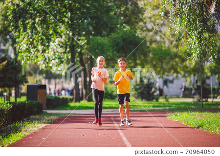 Sports and fitness in adolescence. Caucasian twins boy and girl run on the jogging track in the city park. Two children brother and sister for 10 years running on a rubberized outdoor treadmill Sports and fitness in adolescence. Caucasian twins boy and girl run on the jogging track in the city park. Two children brother and sister for 10 years running on a rubberized outdoor treadmill 70964050