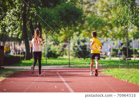 Couple of kids boy and girl doing cardio workout, jogging in park on jogging track red. Cute twins runing together. Run children, young athletes. Teen brother and sister running along path outdoors Couple of kids boy and girl doing cardio workout, jogging in park on jogging track red. Cute twins runing together. Run children, young athletes. Teen brother and sister running along path outdoors 70964318