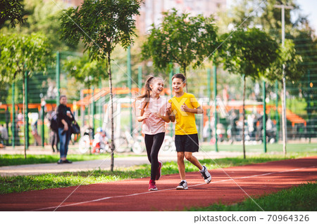 Sports and fitness in adolescence. Caucasian twins boy and girl run on the jogging track in the city park. Two children brother and sister for 10 years running on a rubberized outdoor treadmill Sports and fitness in adolescence. Caucasian twins boy and girl run on the jogging track in the city park. Two children brother and sister for 10 years running on a rubberized outdoor treadmill 70964326