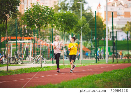 Active recreation and sports children in pre-adolescence. Caucasian twins boy and girl 10 years old jogging on red rubber track through park. Children brother and sister running on treadmill outside Active recreation and sports children in pre-adolescence. Caucasian twins boy and girl 10 years old jogging on red rubber track through park. Children brother and sister running on treadmill outside 70964328