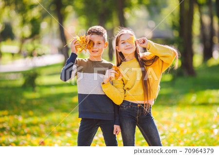 Friendship between siblings. Siblings together outside with bright colored background. Kids autumn portrait. Brother and sister playing in autumn park leaves. Family active fall weekend concept 70964379