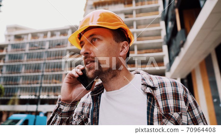 Angry male architect in orange hard hat talks swears on phone at construction site. Builder in plaid shirt emotionally displeased negotiates by cell phone. Screaming stressed architectural designer Angry male architect in orange hard hat talks swears on phone at construction site. Builder in plaid shirt emotionally displeased negotiates by cell phone. Screaming stressed architectural designer 70964408