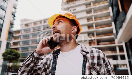 Angry builder, dissatisfied with deadline of work, swears at stress while talking to foreman on phone background of construction site. Wrathful architect, construction engineer talking on cell phone Angry builder, dissatisfied with deadline of work, swears at stress while talking to foreman on phone background of construction site. Wrathful architect, construction engineer talking on cell phone 70964415