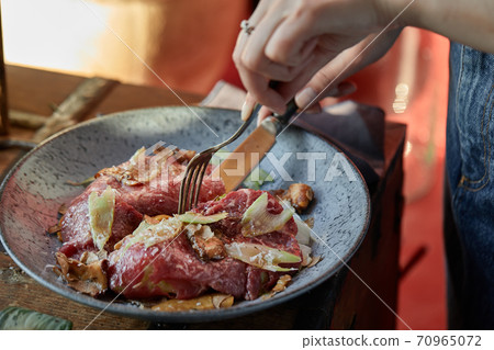 A female hand is preparing a vegetable salad with beef roast beef. A plate of salad with beef roast beef, onions, arugula, pepper and tomatoes on a black table. Top view. 70965072