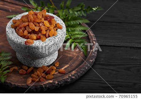 Close up of yellow raisins in a stone bowl, close up, dark background Close up of yellow raisins in a stone bowl, close up, dark background 70965155
