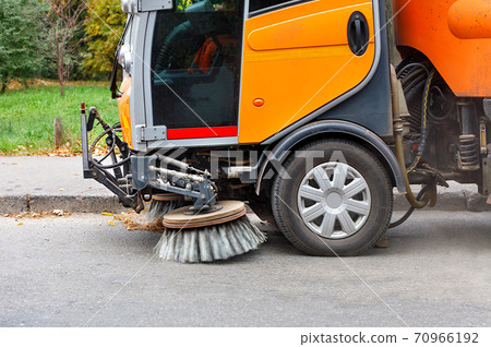 The two rotating front brushes on the sweeping machine sweep the street. 70966192