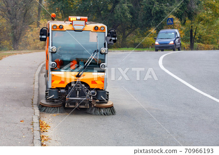 A street sweeper with two front brushes sweeps the street. 70966193