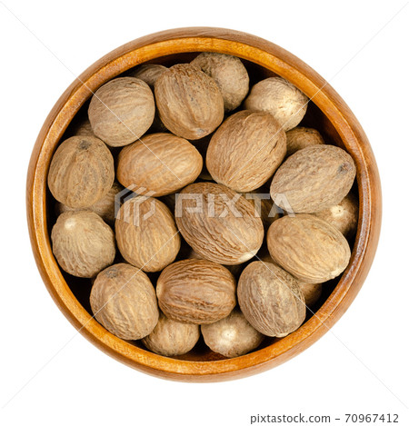 Dried whole nutmegs in a wooden bowl. Fragrant or true nutmeg, seed of Myristica fragrans with distinctive pungent fragrance, used as spice and in traditional medicine. Close-up from above. Food photo Dried whole nutmegs in a wooden bowl. Fragrant or true nutmeg, seed of Myristica fragrans with distinctive pungent fragrance, used as spice and in traditional medicine. Close-up from above. Food photo 70967412