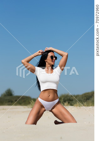 Sensual slim woman sitting on sandy beach 70972960