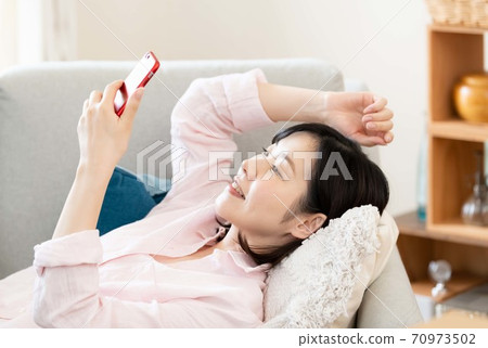 A middle woman looking at a smartphone in the living room A middle woman looking at a smartphone in the living room 70973502