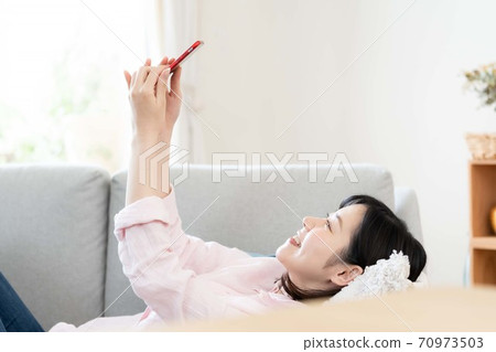 A middle woman looking at a smartphone in the living room A middle woman looking at a smartphone in the living room 70973503