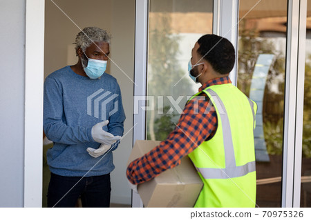 Delivery man delivering package to senior man wearing face mask at home Delivery man delivering package to senior man wearing face mask at home 70975326