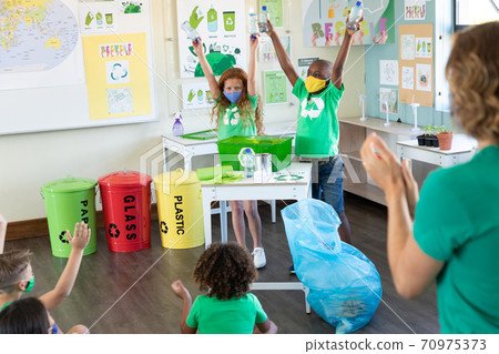 Boy and Girl wearing face masks holding plastic bottles in class 70975373