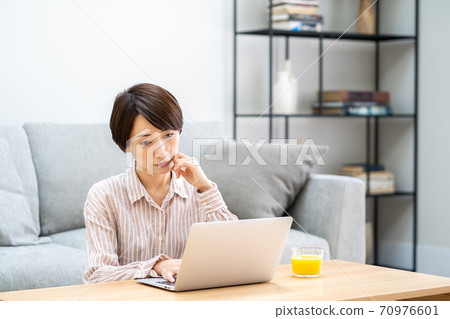 A middle-aged woman teleworking in the living room. A middle-aged woman teleworking in the living room. 70976601