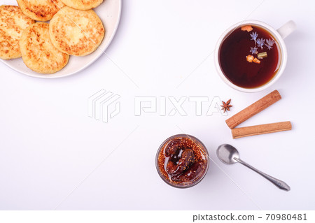 Cottage cheese fritters with fig jam and hot black aromatic tea, Christmas breakfast mood with anise and cinnamon on white background, top view Cottage cheese fritters with fig jam and hot black aromatic tea, Christmas breakfast mood with anise and cinnamon on white background, top view 70980481
