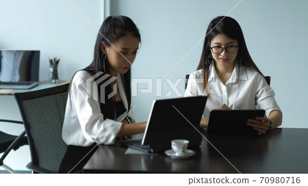 Two female workers consulting on their work with tablet in meeting room 70980716