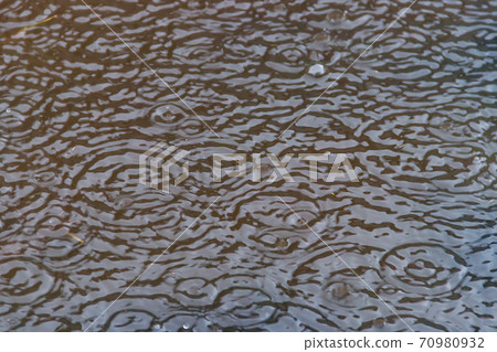 Puddle of water with splashing raindrops during a downpour Puddle of water with splashing raindrops during a downpour 70980932