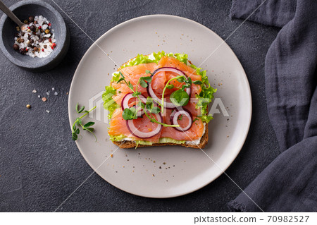 Sandwich with salmon, vegetables and cream cheese on plate. Dark background. Top view. Sandwich with salmon, vegetables and cream cheese on plate. Dark background. Top view. 70982527