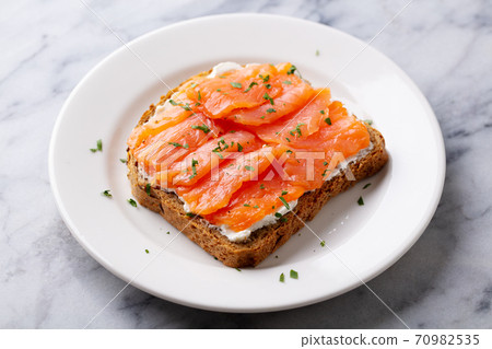Sandwich, toast with smoked salmon and cream cheese on white plate. Marble background. Close up. 70982535
