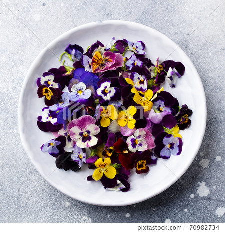 Edible flowers, field pansies, violets on white plate. Grey background. Close up. Top view. 70982734